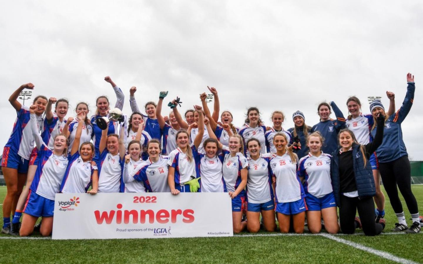 The MIC ladies football team are pictured celebrating. They are dressed in MIC branded football kit and there is a sign that says '2022 Winners'