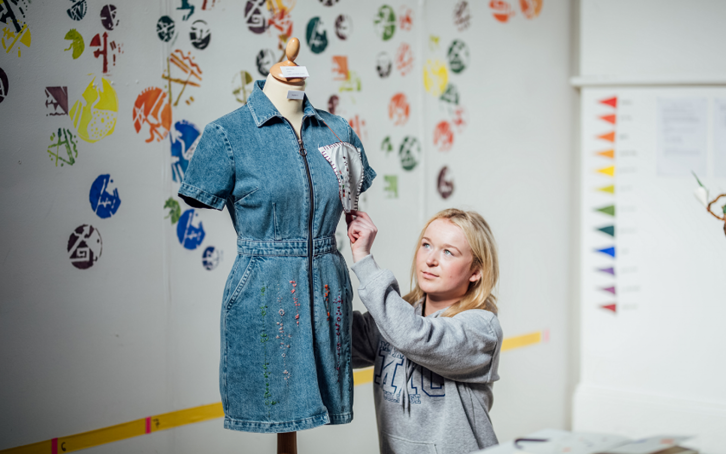 A female student is pictured beside a mannequin. There is a denim dress on the mannequin.. 