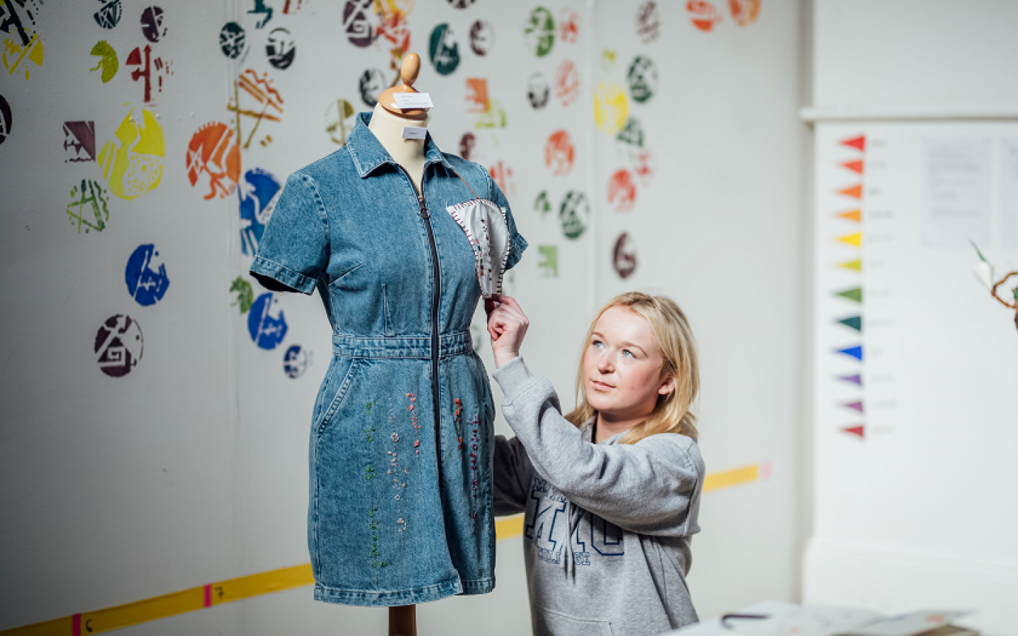 A female student is pictured beside a mannequin. There is a denim dress on the mannequin..