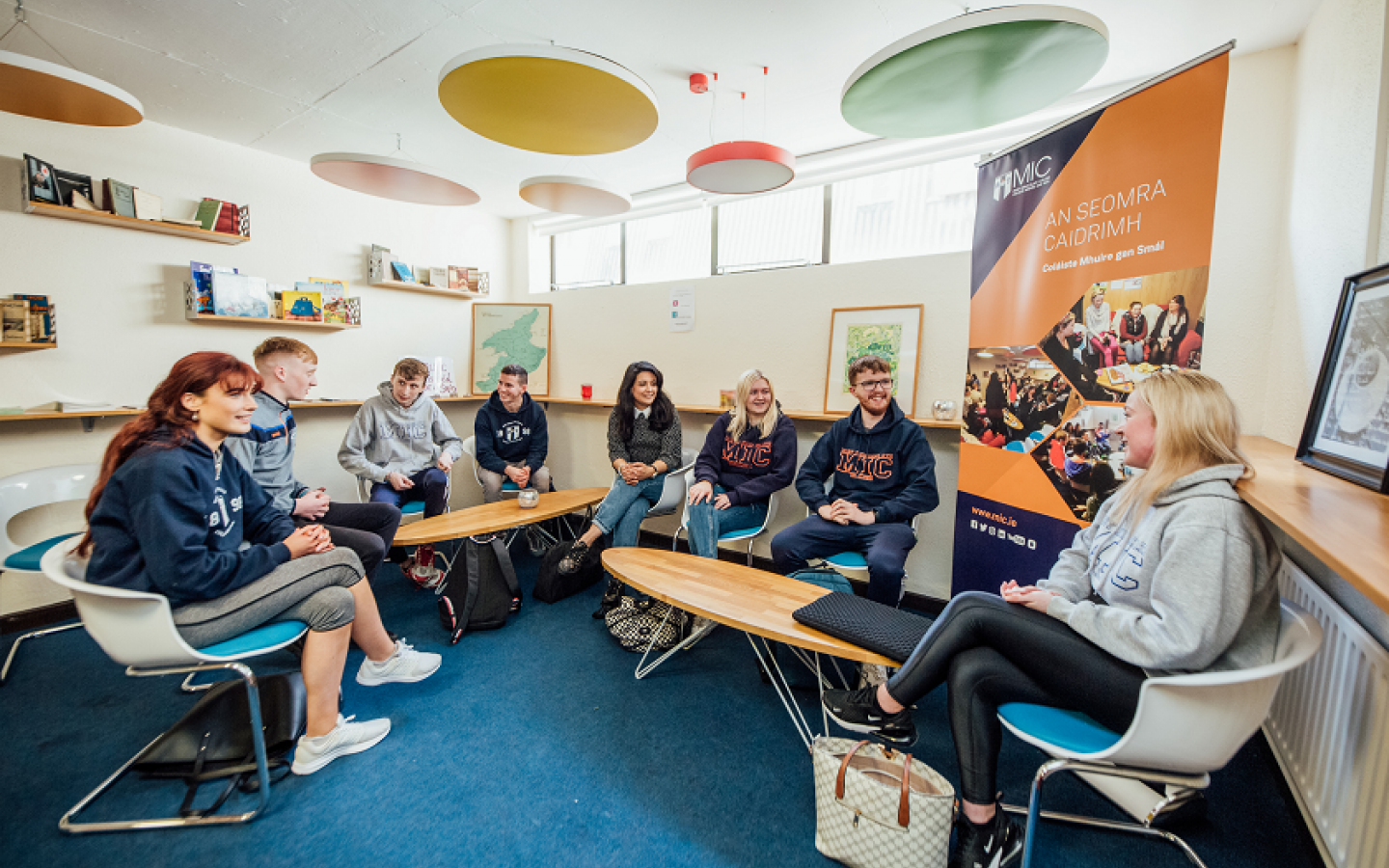 A group of male and female students are pictured chatting in a room.