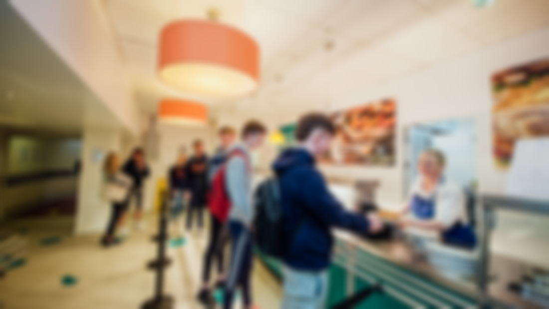 Male and female students are pictured queuing up for food in a canteen