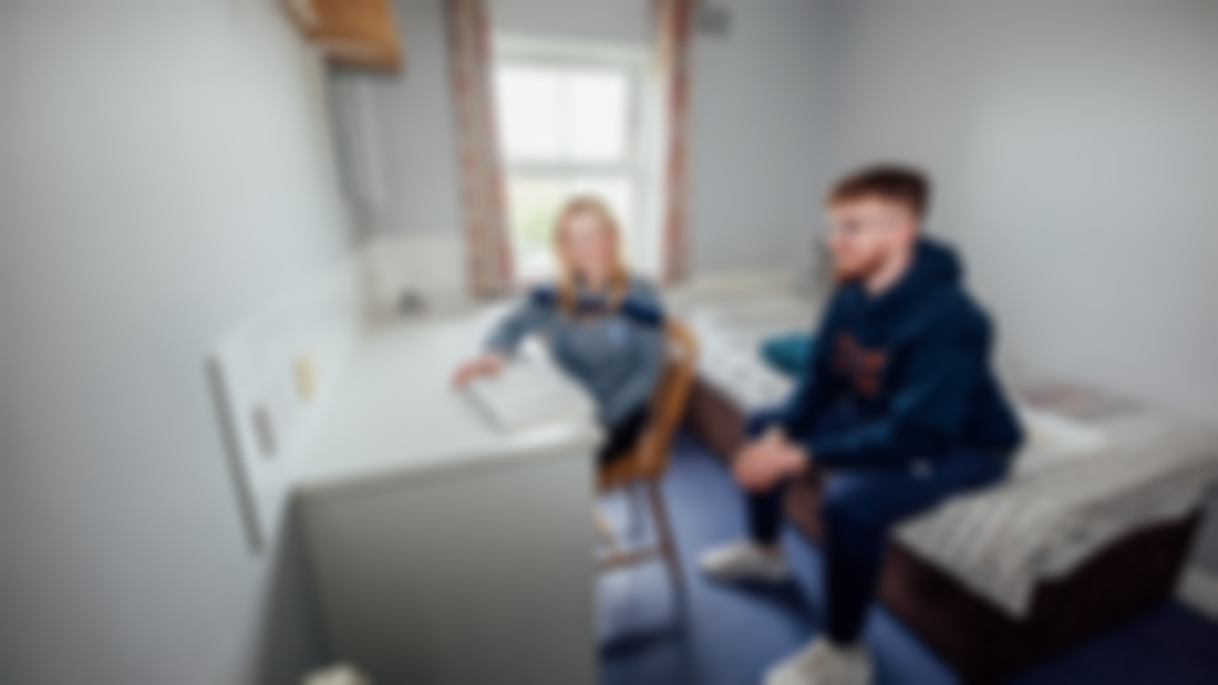 A female student and male student pictured in a bedroom with a desk and bed.