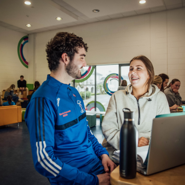 Two students chatting while working on a laptop