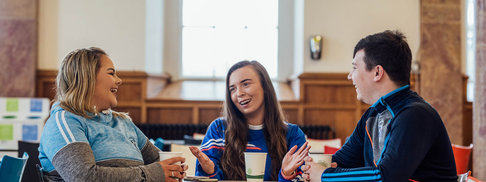 Undergraduate students sitting at a table having coffee, chatting and laughing.