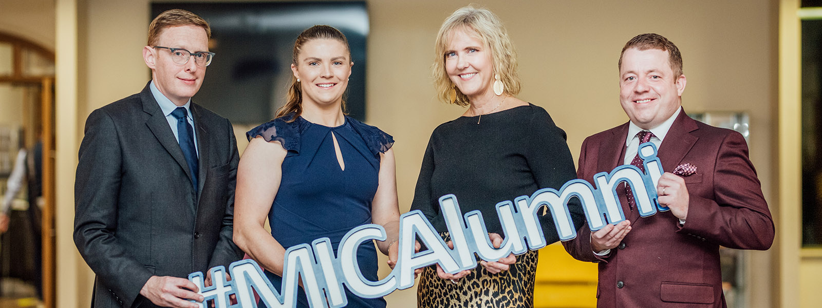 Four 2022 MIC Alumni of the Year Awardees holding a #MICAlumni sign.