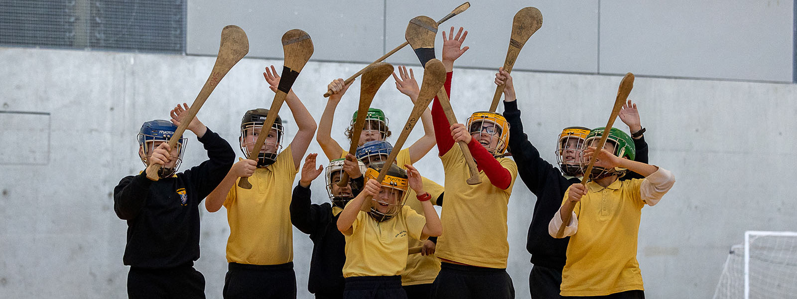 Students at the launch of the MIC Munster GAA Centre of Excellence close together in a group holding hurleys up and reaching for the sliotar.
