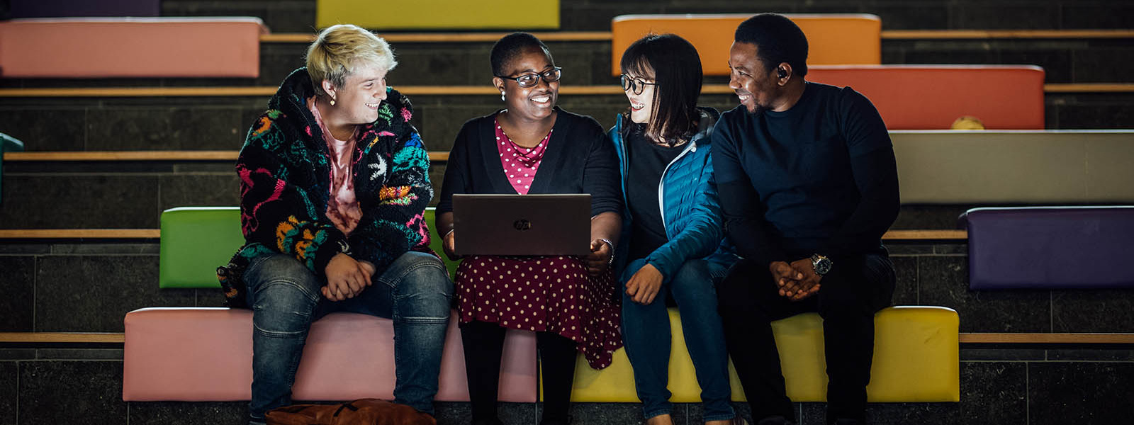 Four postgraduate students sitting on the steps in the tara building looking at a laptop. 