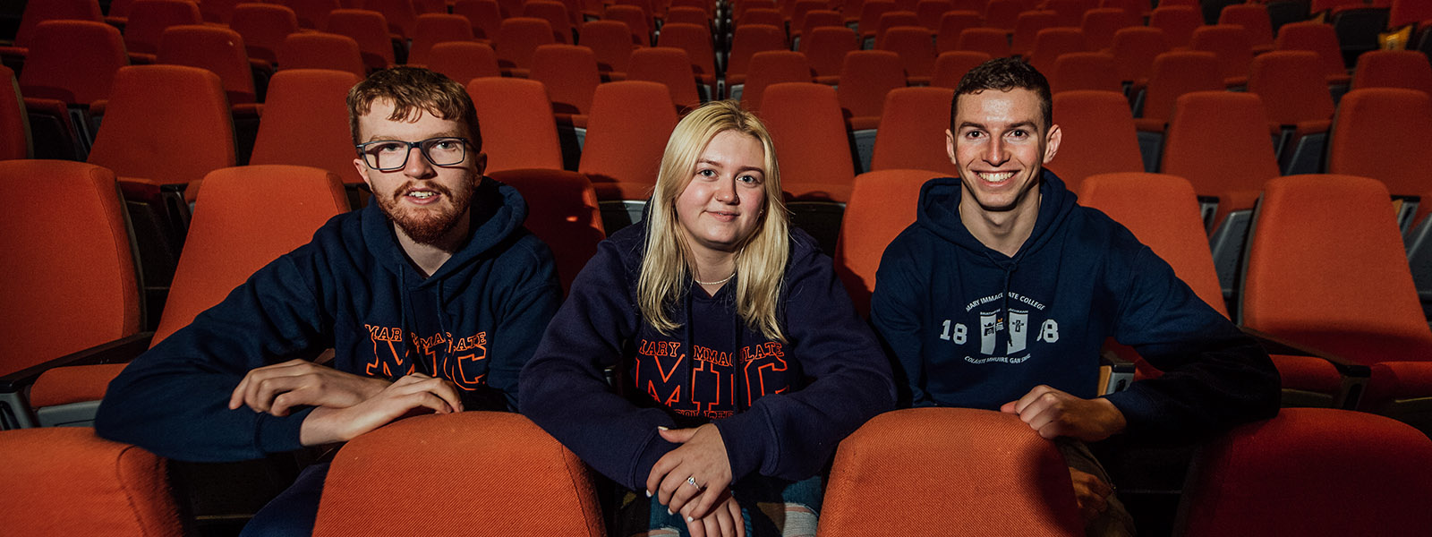 Two male and a female student sitting in theatre chairs