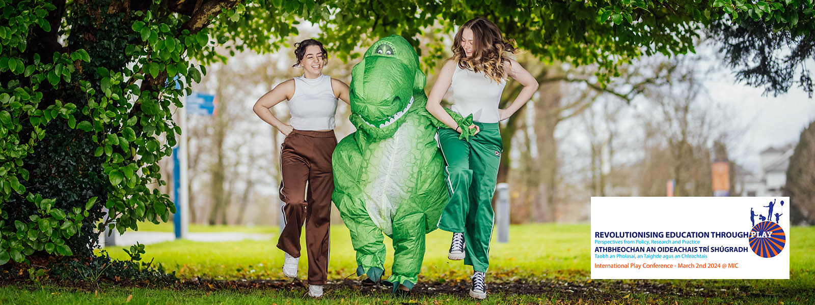 Two women skipping with an inflated green dinosaur on the grounds of MIC