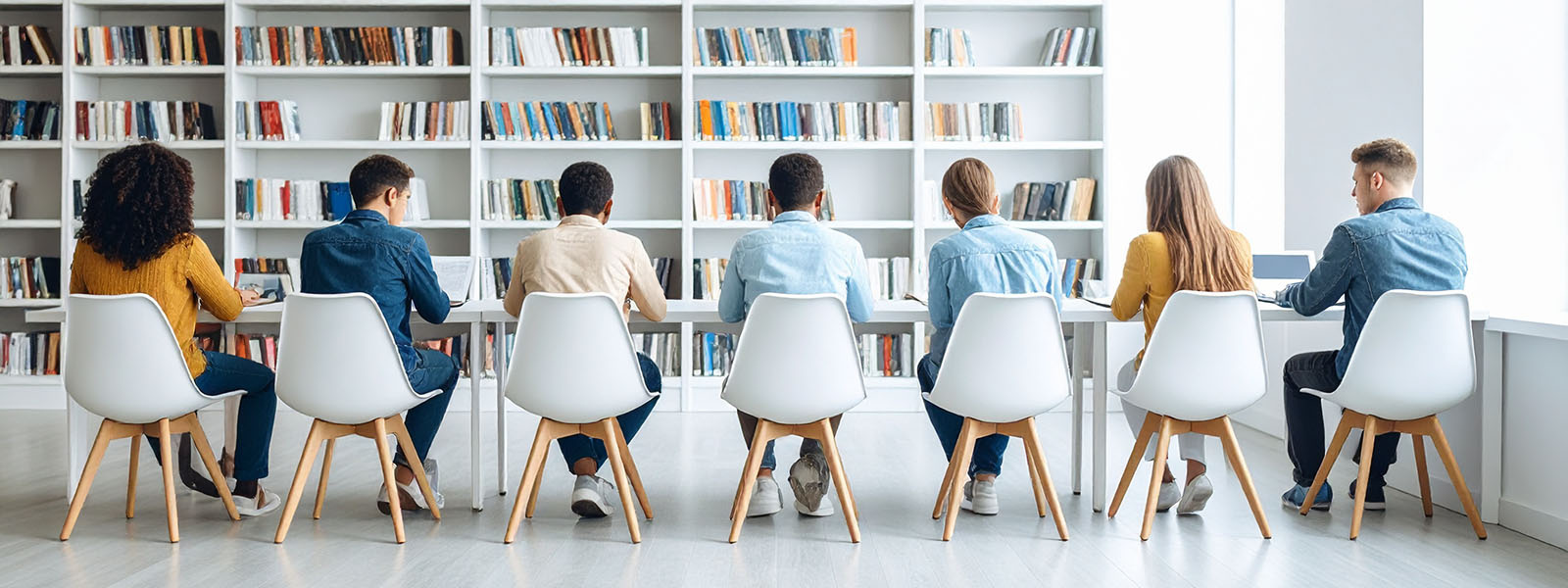 Students sitting at a table in a library with their backs turned to the camera