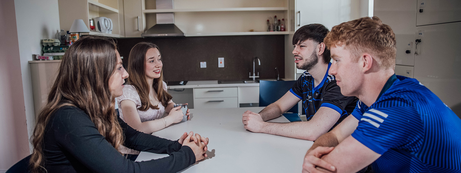 Four students conversing in a joint kitchen area.