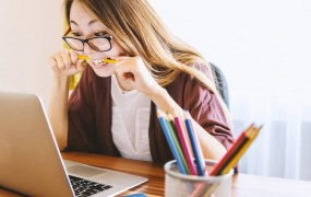 female student sitting in front of a laptop biting on a pencil in frustration