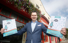 Image of AsIAm CEO Adam Harris holding the new resource outside a Supervalu shop