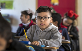 A child sitting in a classroom holding a pencil 