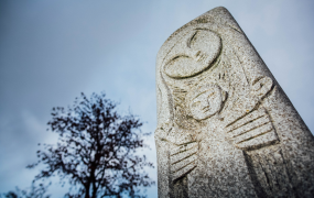 An Imogen Heap sculpture of the Virgin Mary stands beside a tree without leaves against a grey sky