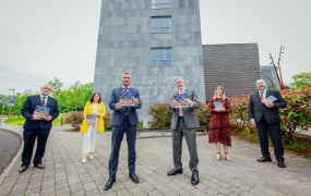 Four men and two women pictured outside the Lime Tree Theatre each holding a copy of the MIC Doctoral Framework booklet