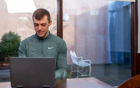 Male student wearing a green half zip Nike top smiles while looking at a laptop screen