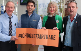Three men and one woman pictured holding an orange sign that says '#IChooseFairtrade'