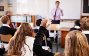 Student raising arm in front of teacher at top of the class 
