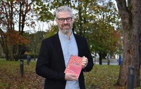 Dr John Morrissey holding a copy of his book