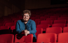 Liam pictured sitting in red theatre seats with dark atmospheric background