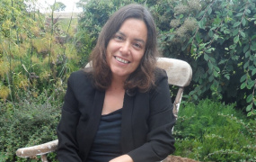 Sara Ahmed sitting in a chair in a garden with green shrubs behind her