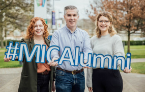 Three alumni holding an MICAlumni card