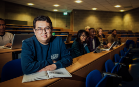 Male student sitting in lecture hall with other students behind him