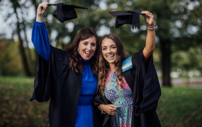 Two female graduates holding their graduation caps above their heads