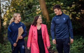 Professor Niamh Hourigan pictured with Niamh Murphy and Diarmuid Ryan walking in a wooded area. Diarmuid and Niamh are carrying hurleys.