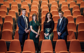 Declan, Petula, Miriam and Tomás standing in a theatre with orange chairs