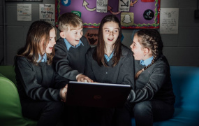 Three female and one male student looking excited and surprised at laptop screen