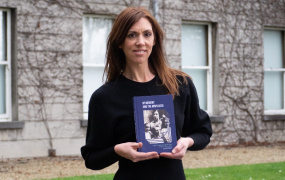Sarah O'Brien holding her book in front of College building