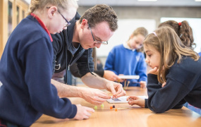 Male teacher helps two students, one male and one female, with a task at a desk