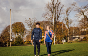 Diarmuid Ryan and Niamh Murphy walking on a GAA pitch and holding hurleys