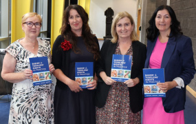 Four women standing and posing for a photo, each holding a copy of the same book that was launched at the event