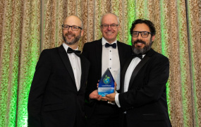 Three men posing for a picture holding an award