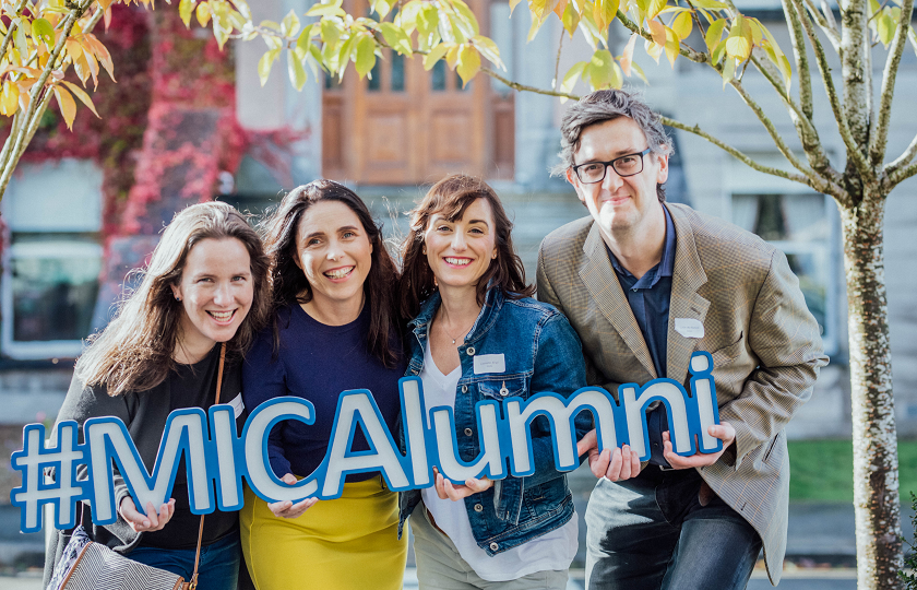 4 MIC graduates holding MICAlumni sign