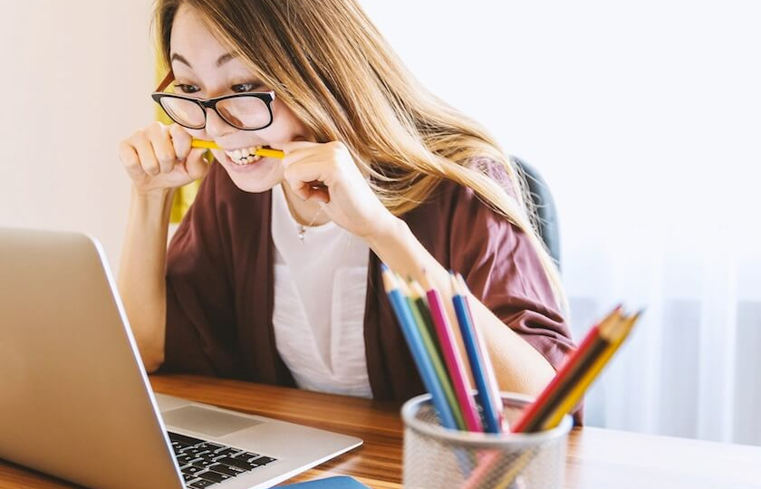 female student sitting in front of a laptop biting on a pencil in frustration