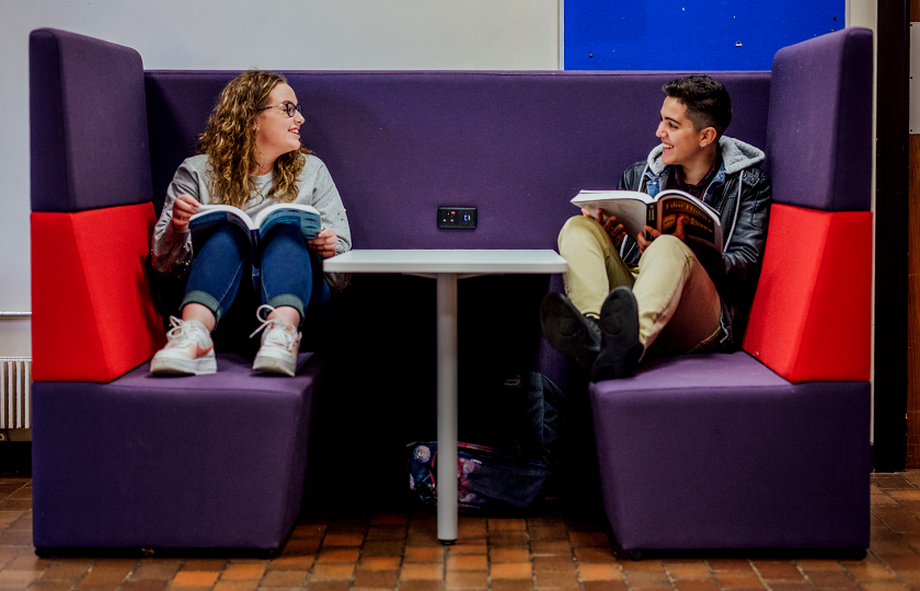 Two students sitting at a table holding books