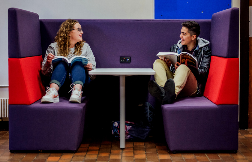 Two students sitting at a table holding books 