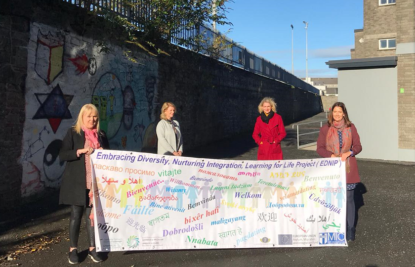 Four women holding a banner on the grounds of a school 