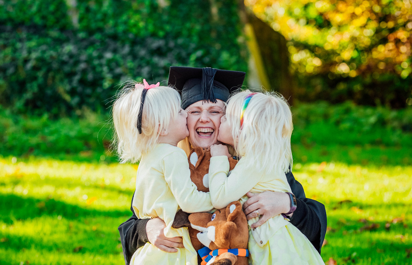 Woman in graduation robes hugs her two daughters 