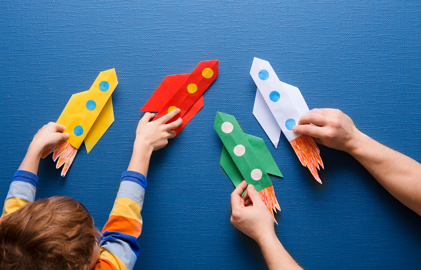 Child and adult playing with paper rockets against a blue backdrop