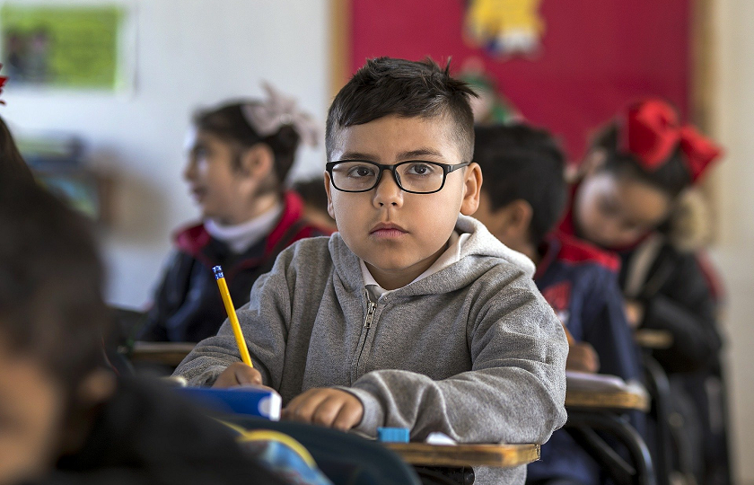 A child sitting in a classroom holding a pencil 