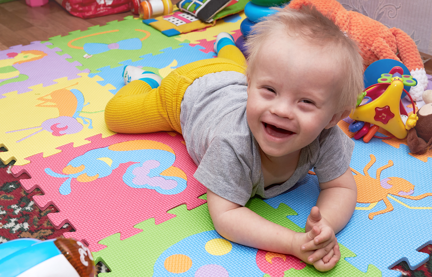 Stock image of a male child with mixed abilities plays on a colourful soft play mat 