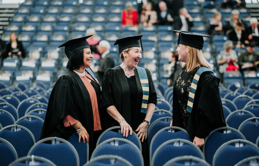 Three female graduating students standing beside a row of chairs