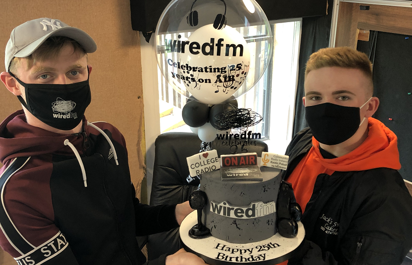 Two male students wearing masks holding a birthday cake and a balloon 