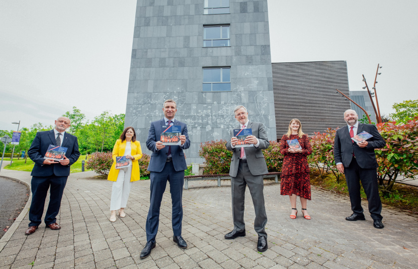 Four men and two women pictured outside the Lime Tree Theatre each holding a copy of the MIC Doctoral Framework booklet