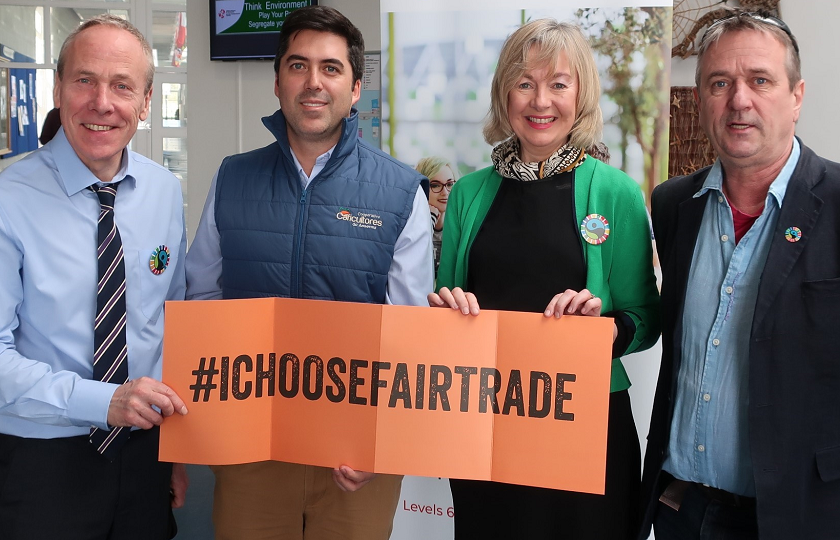 Three men and one woman pictured holding an orange sign that says '#IChooseFairtrade'